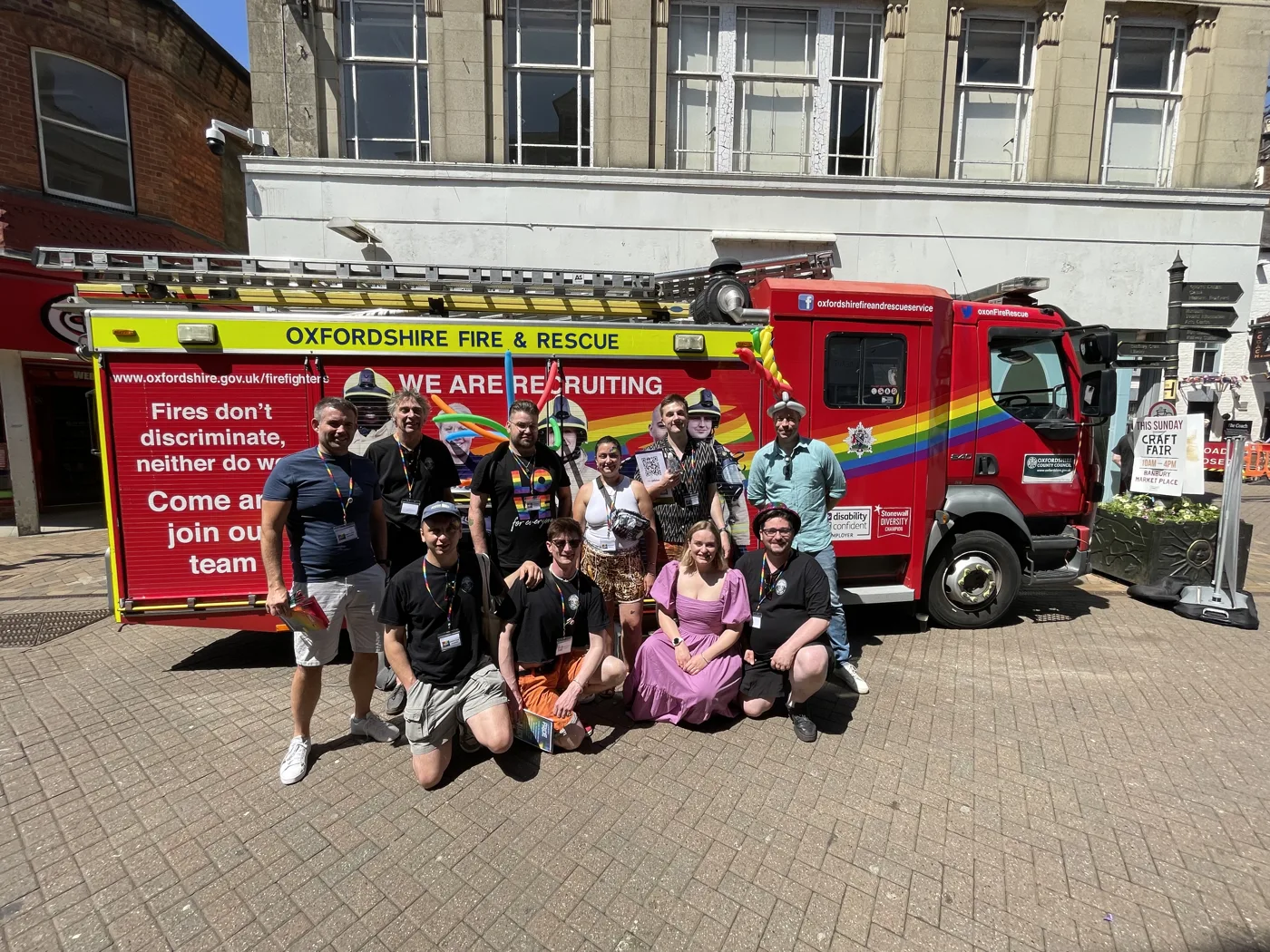 A group of people posing in front of an Oxfordshire Fire and Rescue engine with rainbow livery and the slogan Fires don't discriminate, neither do we