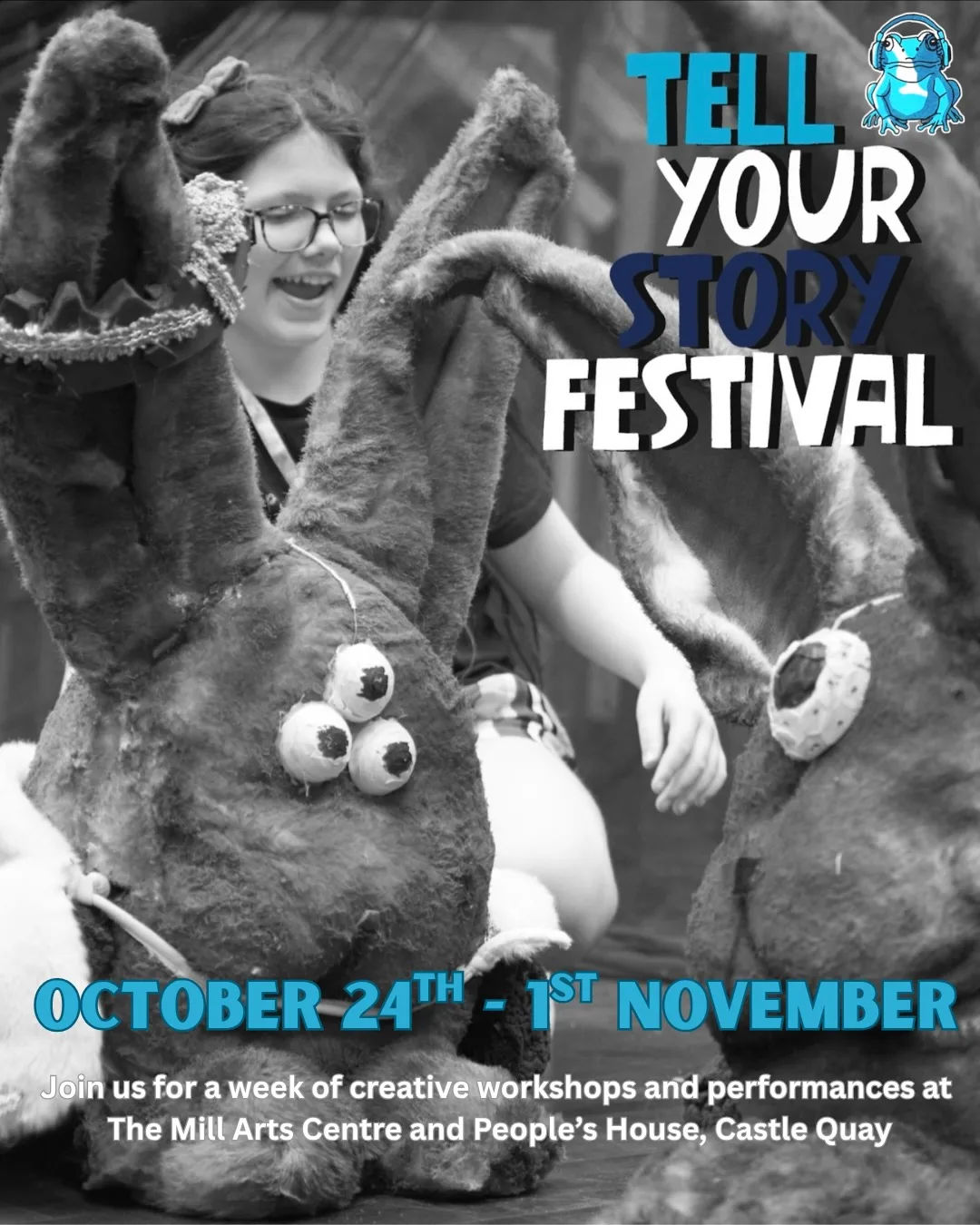 A young person in glasses smiling behind two large rabbit puppets with button eyes, under the Tell Your Story Festival logo